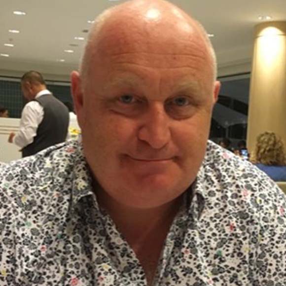 Portrait of a bald man wearing a floral-patterned shirt in an indoor setting with soft lighting.