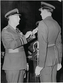 Black and white photograph of a military officer in uniform presenting a medal or pin to another uniformed individual during a formal ceremony.