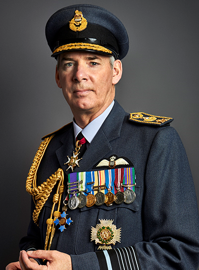 A distinguished man in full military uniform, adorned with medals and decorations, wearing a peaked cap, posing against a neutral background.