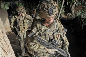 Soldiers in military uniform carrying equipment while moving through a narrow trench during an operation, representing the experiences of armed forces personnel.