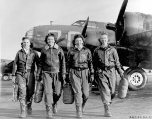 Historic black and white photograph of four women in military flight suits walking in front of an aircraft, representing the role of women in wartime service.
