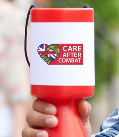 Hand holding a red donation collection bucket with the Care After Combat logo on the front, used for fundraising to support veterans in the justice system.