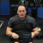 Man using an indoor rowing machine during a fitness training session, wearing a black sports shirt in a gym environment.