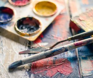 Close-up of paintbrushes, palette knives, and vibrant paints on a canvas, representing creativity and artistic tools for World Art Day.